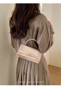 Detailansicht der cremefarbenen Handtasche mit Krokodilprägung und silbernem Drehverschluss
