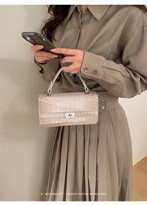 Detailansicht der beigefarbenen Handtasche mit Krokodilprägung und silbernem Drehverschluss