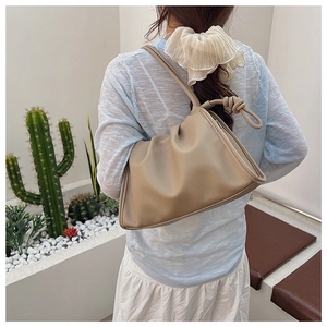 Detail of a beige pleated shoulder bag featuring unique knotted strap on a female model
