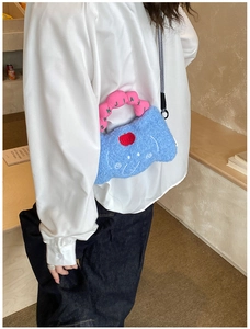 Blue plush crossbody bag with cartoon face and red apple embroidery worn by model