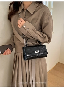 Detail einer schwarzen Handtasche mit Krokodilmuster, Silberschnalle und Kettenriemen