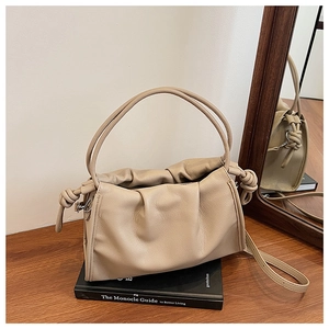 Détail d'un sac nuage plissé beige en cuir souple avec poignée nouée sur une table en bois
