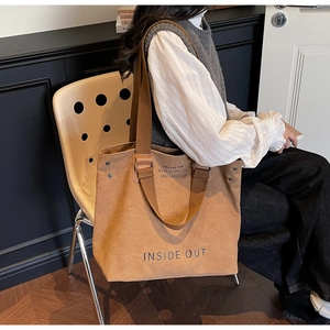 Detail of a brown canvas tote bag featuring large text print and leather strap accents