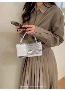 Detail der weißen Handtasche mit Krokodilmuster und elegantem Metall-Drehverschluss