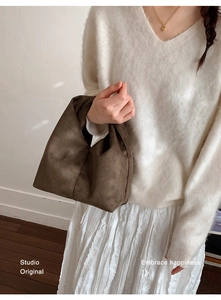 Detail of soft brown suede cloud bag held by hand, showing textured pleated material