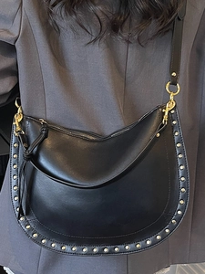Fashionable black leather half-moon crossbody bag with gold rivets on a grey suit model