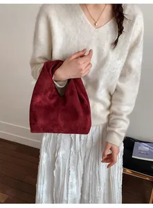 Detail of a minimalist wine red suede pleated handbag held by a model in casual outfit