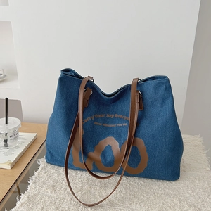 Detailed close-up of dark denim tote bag featuring brown leather handles and text printing