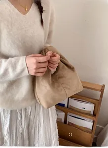 Detail of minimalist suede ruched cloud handbag in earth tone held by a model