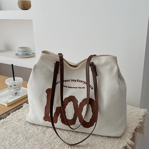 Detail of canvas tote bag with brown leather handles and decorative artistic lettering