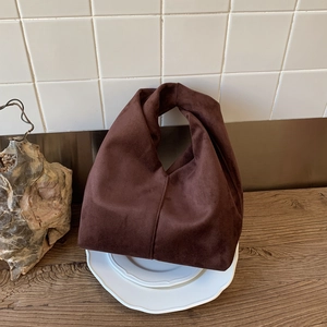 Detailed view of dark brown suede knotted handbag on a ceramic plate background
