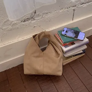 Detail of khaki suede handbag featuring a stylish knotted handle on a wooden floor
