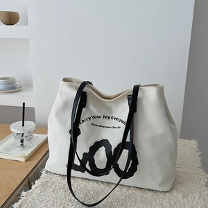 White canvas tote bag detail with black leather straps and stylish text typography
