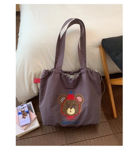 Detail view of purple embroidered bear tote bag with drawstring closure in a cozy setting