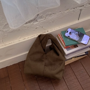 Detail of a brown suede cloud bag featuring a unique knotted handle and pleated texture