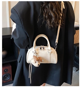 Detail of cream crossbody pillow bag with cute plush bear charm on a black blazer