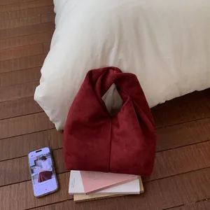 Detail view of red suede cloud bag with knotted handle on wooden floor setting