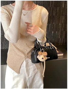 Close-up of black leather bowling handbag with silver zipper and cute plush bear charm
