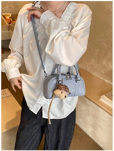 Detail of light blue mini Boston bag with plush puppy pendant and slim crossbody strap