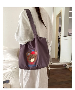 Detail of purple canvas tote bag featuring cute cartoon bear embroidery and drawstring
