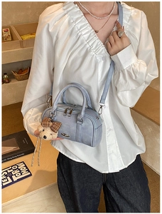 Detail view of a light blue Boston bag with a teddy bear charm and brown plaid bow