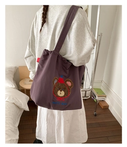 Detail of purple canvas tote bag featuring a cute brown party bear embroidery and wide strap