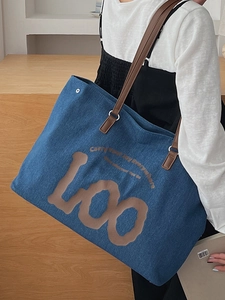 Large blue denim tote bag with brown leather straps and artistic lettering for daily use