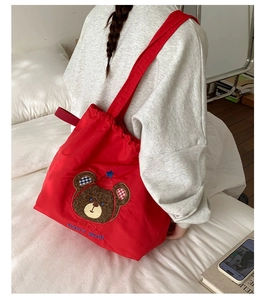 Detailed back view of model wearing a red tote bag with bear embroidery and drawstrings