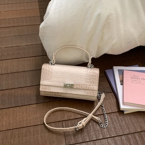 Detail der cremefarbenen Handtasche mit Kroko-Prägung und silbernem Drehverschluss