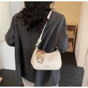Rear view of model wearing white minimalist underarm bag with cute bear charm