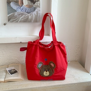 Detail of red canvas tote bag featuring embroidered party bear and white drawstring closure