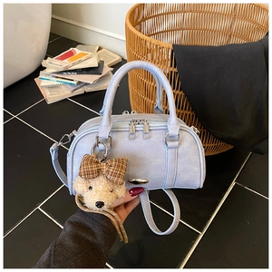 Detail of light blue leather Boston handbag with silver emblem and cute bear charm accessory