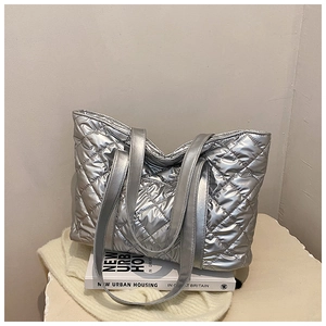 Détail d'un sac cabas argenté matelassé à motif losanges posé sur des livres