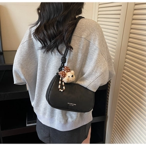 Detail of black hobo bag with white brand lettering and cute plush bear keychain