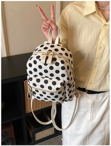 Detailed macro view of white canvas backpack with black polka dots and metal zippers