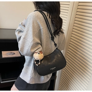 Detail of black leather crescent bag with thin shoulder strap and bear plush charm