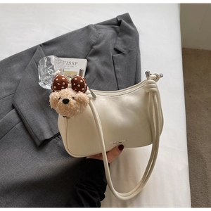 Detail of cream white underarm bag with metal buckle and teddy bear charm on grey blazer