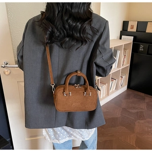 Brown suede crossbody bag worn with a grey blazer in a stylish home interior setting