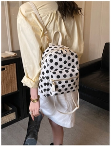 Lifestyle shot of a white backpack with black polka dots featuring golden zippers