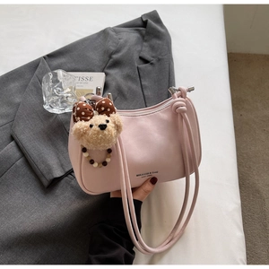 Detailed close-up of pink leather curved handbag featuring a cute plush bear charm
