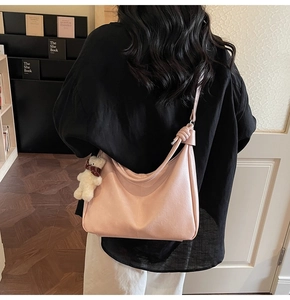 Detail of pink hobo shoulder bag with a knotted strap and cute plush bear charm accessory