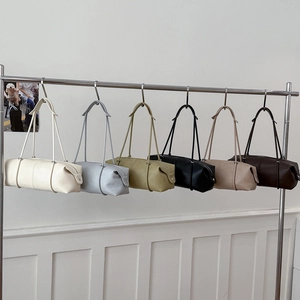 Multiple colors of cylindrical leather tote bags hanging on a silver metal bar