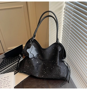 Détail du sac cabas noir avec motifs étoiles argentées et lettrage embossé avec breloque en cuir