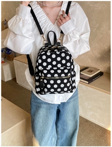 Lifestyle shot of woman wearing a black mini backpack with white polka dots pattern