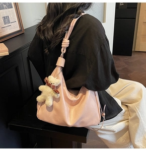 Detail of pink hobo bag featuring a decorative knot strap and a cute teddy bear charm