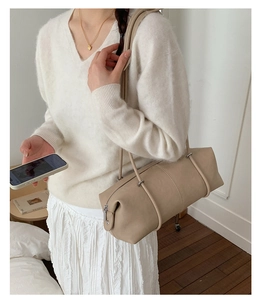 Detail view of a beige minimalist bolster bag with smooth texture and metal zipper detail