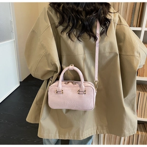 Detail view of the pink suede small square bag worn crossbody on a khaki jacket