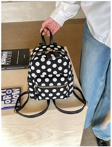 Detail view of mini black polka dot canvas backpack with front zipper pocket and strap