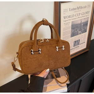 Close-up of brown suede Boston bag with silver bone charm and embossed side logo