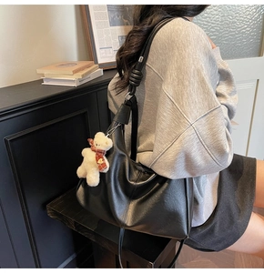 Detail of black large hobo bag with knotted strap and a small plush bear charm